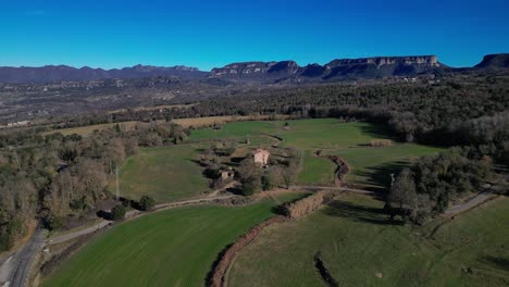 Tavertet-region-with-lush-fields-and-scenic-mountains-under-clear-blue-sky,-aerial-view