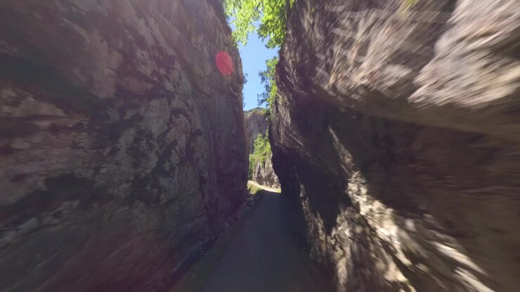 Un volo cinematografico a bassa quota attraverso una stretta gola calcarea con una strada e un fiume, che mostra l'autentica bellezza naturale delle Asturie, Spagna