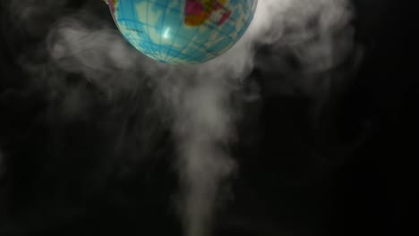 the simulated earth spins above steam smoke that shot up on a black background. concept of earth destroyed by pollution.