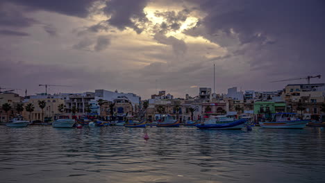 blue white boats anchored in port town as sun sets over marsaxlokk, malta, timelapse