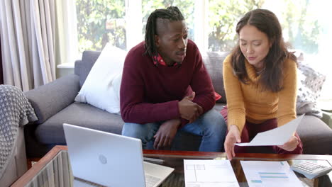 Serious-diverse-couple-with-laptop,-discussing-domestic-finances-at-home,-copy-space,-slow-motion