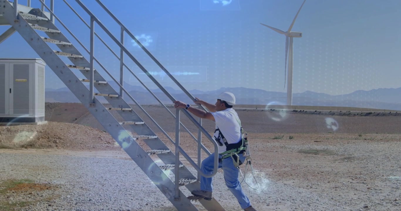 Tech walking to metal stairs on wind farm, placing hand on rail, climbing while wearing harness