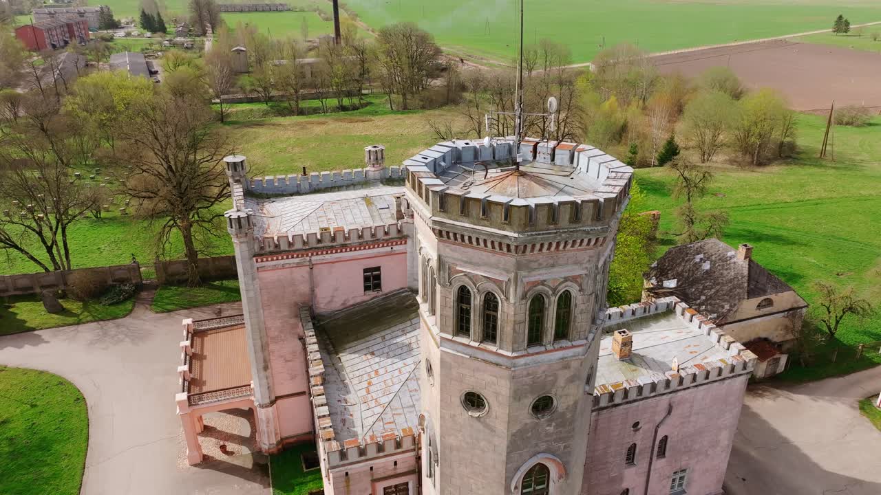 Historic Vecauce Palace with towers and pink facade stands in Latvian landscape