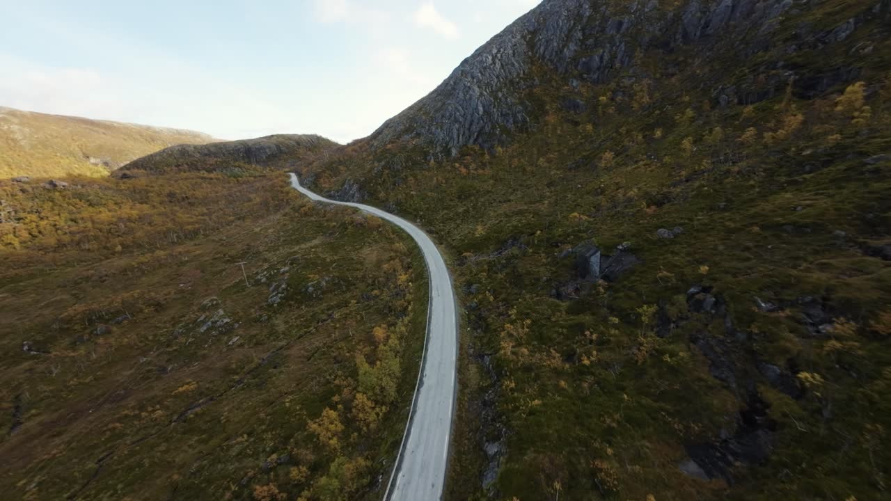 Droneoptagelse, der dykker ned fra oven og følger en vej i efteråret i Nordnorge.