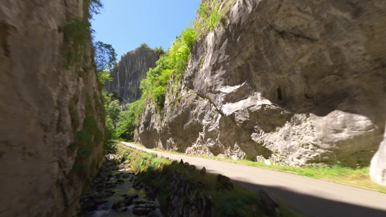 Ein dynamischer Drohnenflug in geringer Höhe folgt einem Gebirgsfluss durch eine steile Kalksteinschlucht unter einer Brücke in Asturien, Spanien. Zeigt authentische Natur und umweltfreundliche Reisethemen.