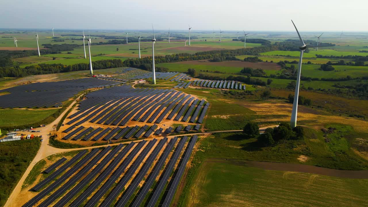 Aerial footage of solar panels plant and wind turbines in a wind farm generating green electric energy on a wide green field on a sunny day, in Taurage, Lithuania, pan right