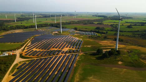 aerial footage of solar panels plant and wind turbines in a wind farm generating green electric energy on a wide green field on a sunny day, in taurage, lithuania, pan right