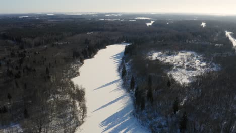 Long-Frozen-Lake-Between-Dense-Forest-On-A-Sunny-Day-At-Wintertime