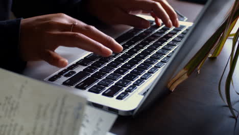 camera pushes in on a woman typing on her laptop computer sitting next to a notebook with hand written notes in it