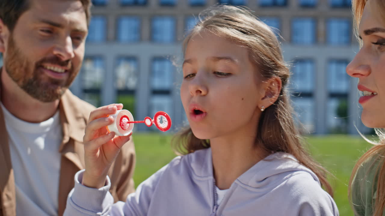 Cheerful girl playing soap bubbles at greenery neighbourhood picnic closeup