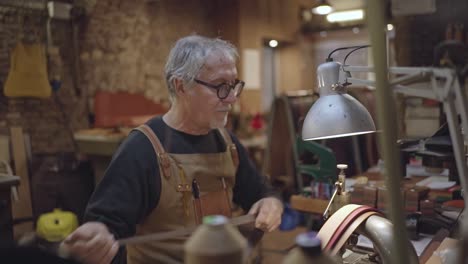 side-view-in-slow-motion-of-leather-craftsman-sitting-while-sewing-leather-belt