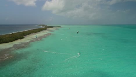grupo de kitesurfistas cabalgando y deslizándose sobre aguas turquesas, salina los roques