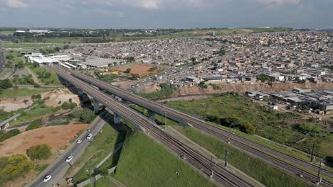 4K-aerial-clip,-a-static-drone-captures-the-dynamic-energy-of-a-high-speed-train,-juxtaposed-against-the-bustling-highways-and-the-expansive-urban-township-of-Alexandra-in-Johannesburg,-South-Africa