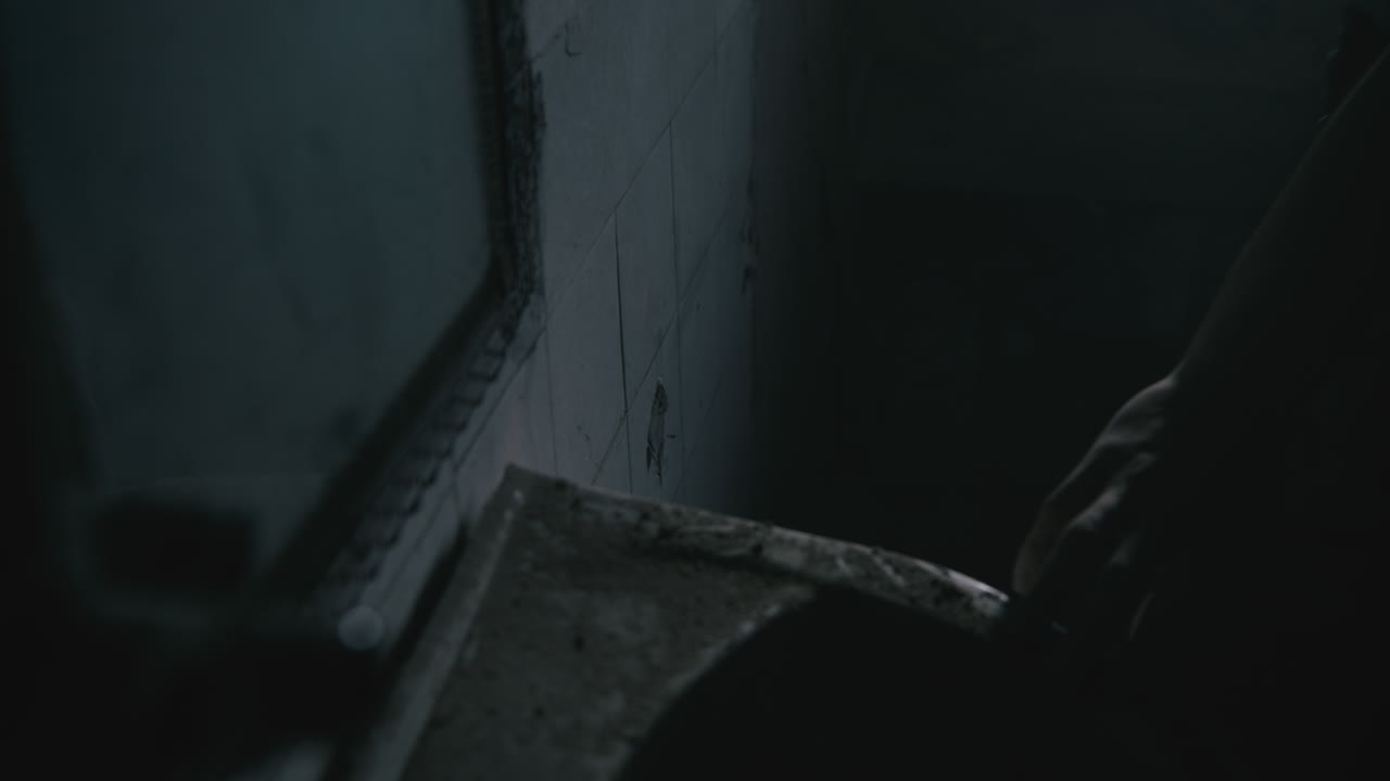 Pale bald skinny man sits next to the wall in the creepy old bathroom at night