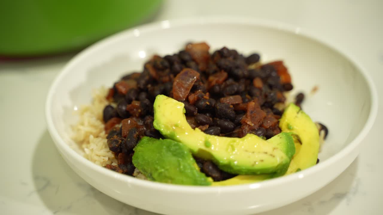 Medium shot of rice topped with bean stew and avocado slices in a bowl
