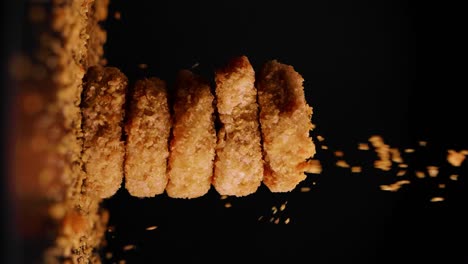 vertical shot of spinning vegan chicken nuggets with falling crumbs in static shot against black background