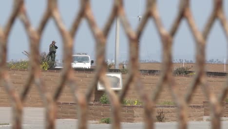 a border patrol agent is viewed through the border fence from mexico