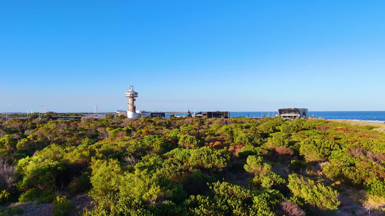 Aerial footage captures the Queenscliff Lighthouse amidst lush greenery and coastal views under clear blue skies in Bellarine, Victoria