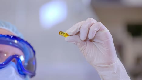 una trabajadora farmacéutica que examina una cápsula de gel de naranja en un laboratorio