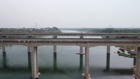 highway bridge built over the river basin in the indian rural terrain, slow motion, drone shot