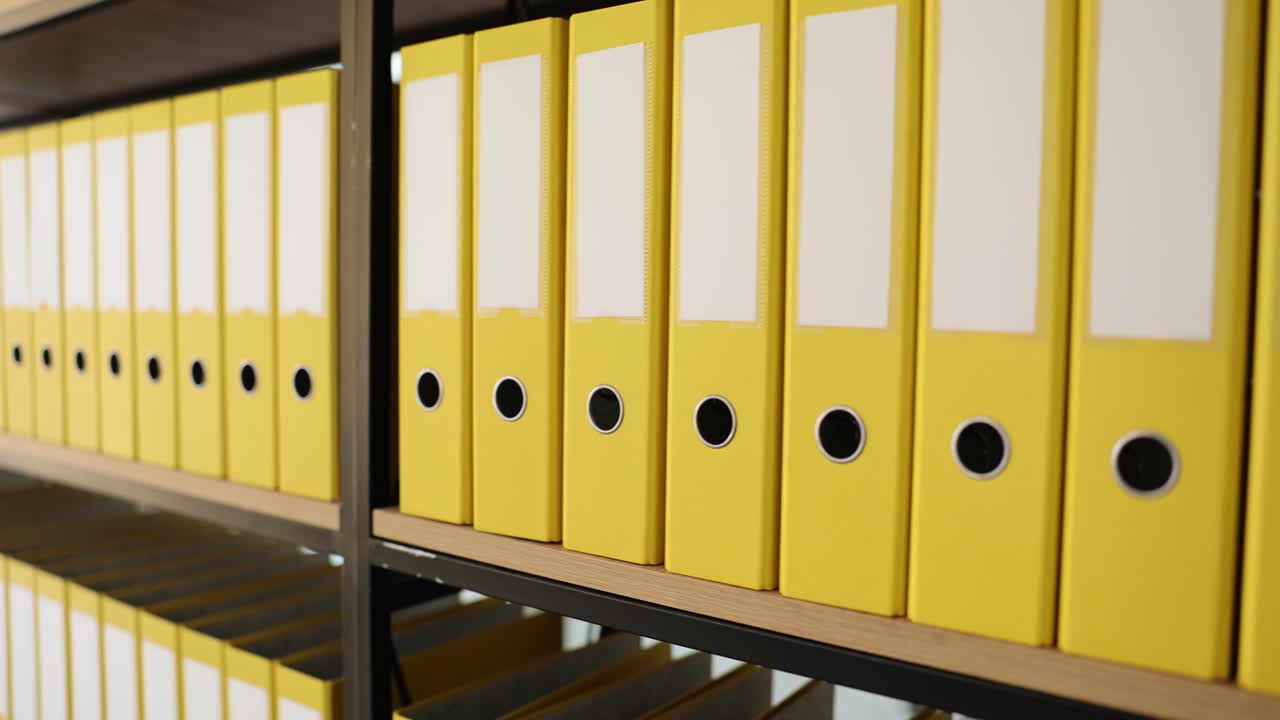 Žluté složky s materiály uspořádané na polici regálu.