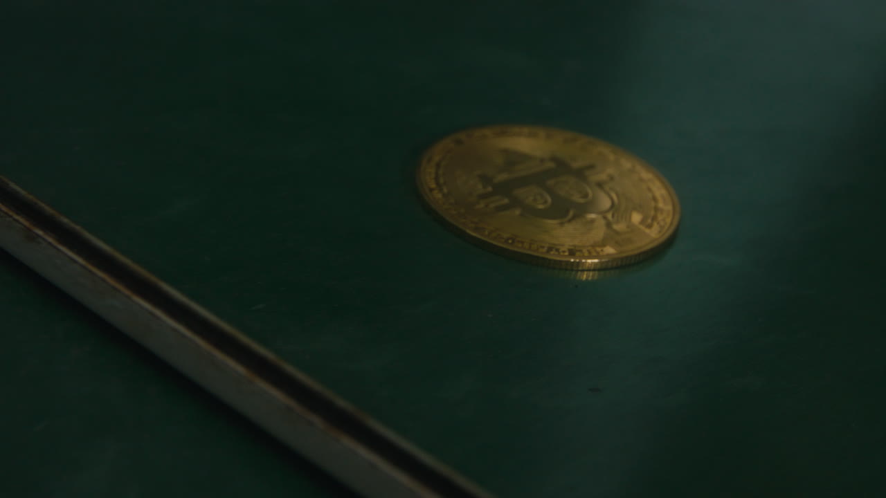 A bitcoin coin lies on a dark green surface as the camera glides past, eventually revealing its mirrored reflection—suggesting duality, value perception, and the intangible nature of digital currency