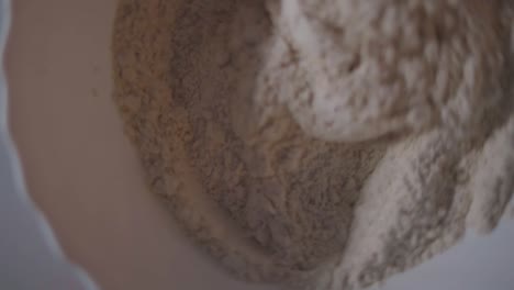 female mixing flour with a spoon in a white bowl while the camera is turning from above