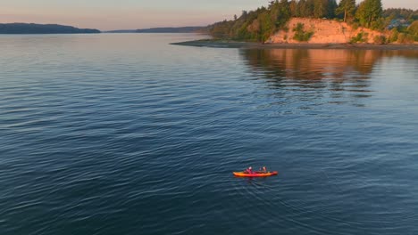 aerial drone shot circling young couple sea kayaking paddling in bay to then reveal southworth ferry terminal pier near seattle washington at sunrise