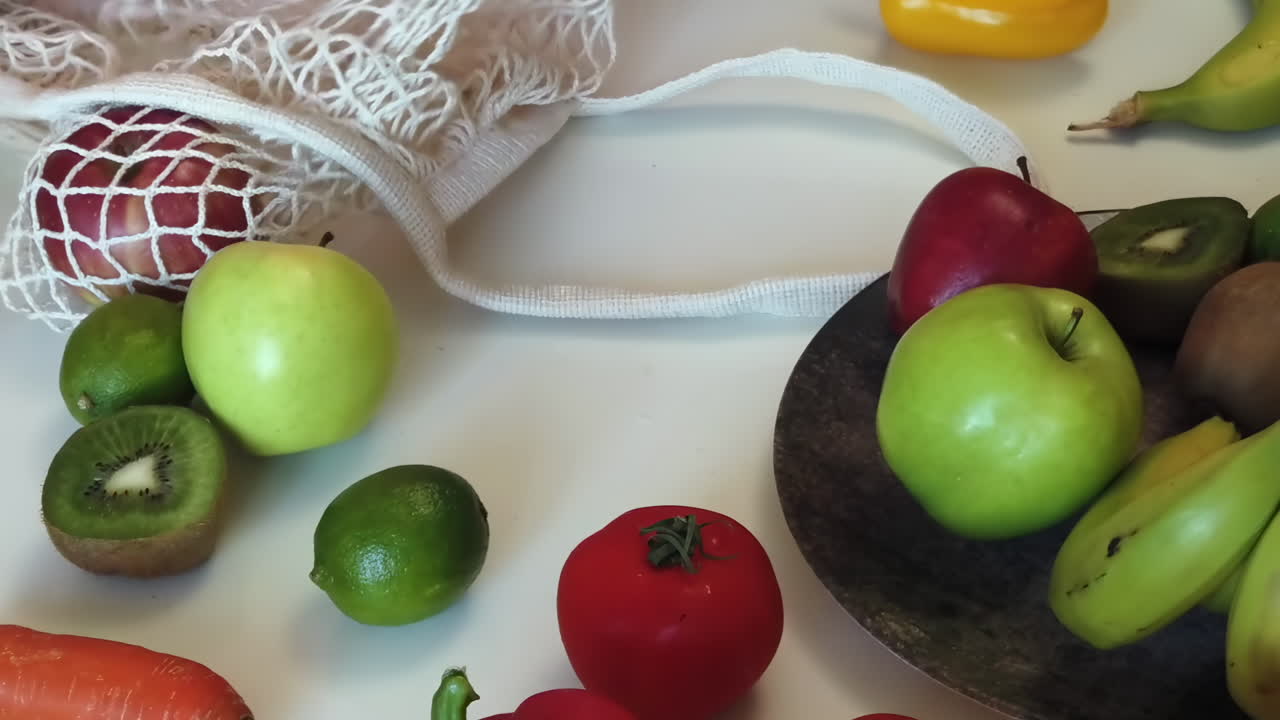 Close up of a woman placing apples in a bowl on a table near other fruits and vegetables