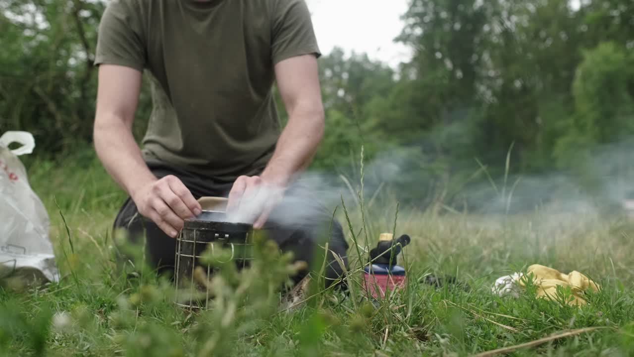 Caucasian male beekeeper in protective clothing preparing smoker. apiary and honey making, small agricultural business and hobby.