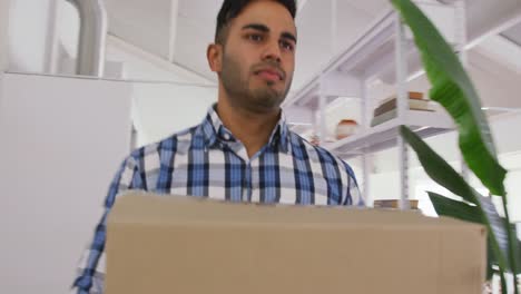 hombre de raza mixta moviendo una caja de cartón a una nueva oficina creativa