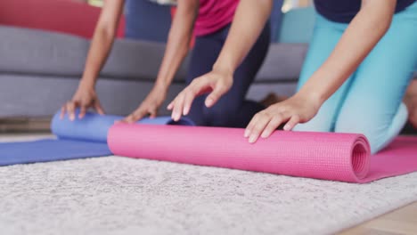 video of midsection of diverse female friends rolling yoga mats at home