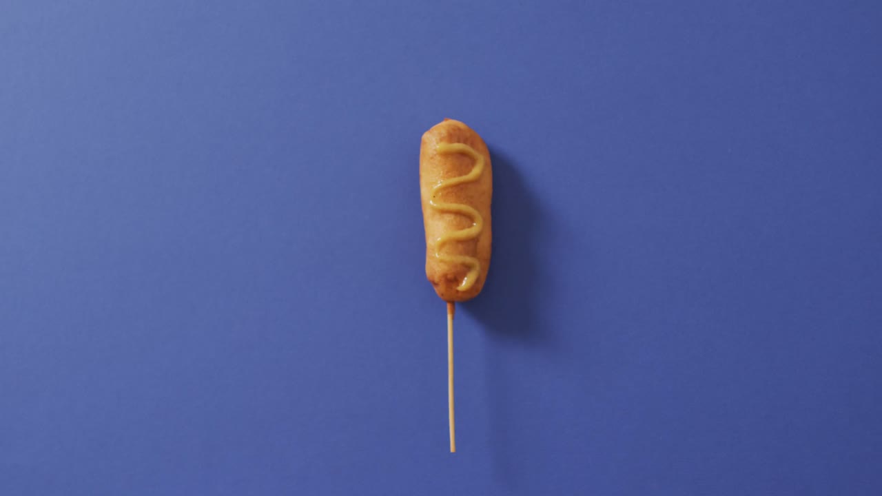 video de un perro de maíz con mostaza en una superficie azul