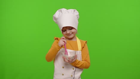 child girl kid dressed as professional cook chef stir flour in plate, smiling, showing thumb up