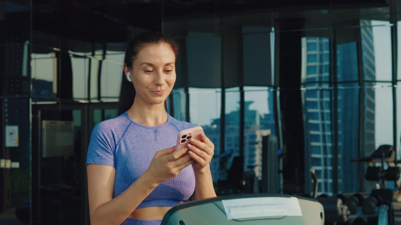 Woman using smartphone on treadmill in gym