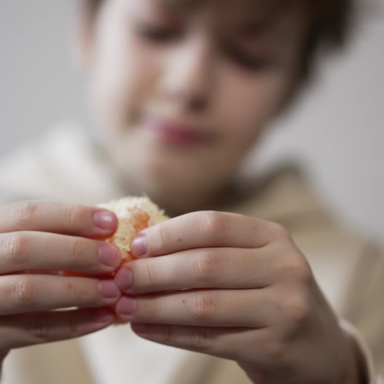 Unknown boy peeling the tangerine in front of camera. Teenager rips the fruit into pieces ready to eat. Close up. Blurred backdrop