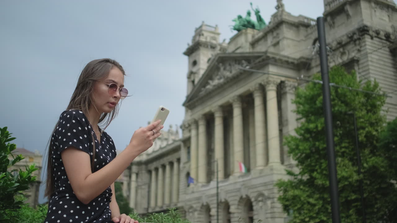 역사적인 건물 앞에서 전화를 사용하는 젊은 여성