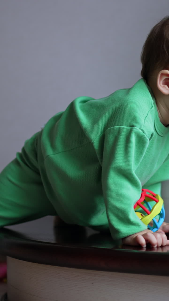 Caucasian toddler with pacifier in mouth sits on the stairs. Kid takes a toy, drops a pacifier and pulls the toy to the mouth. Vertical video