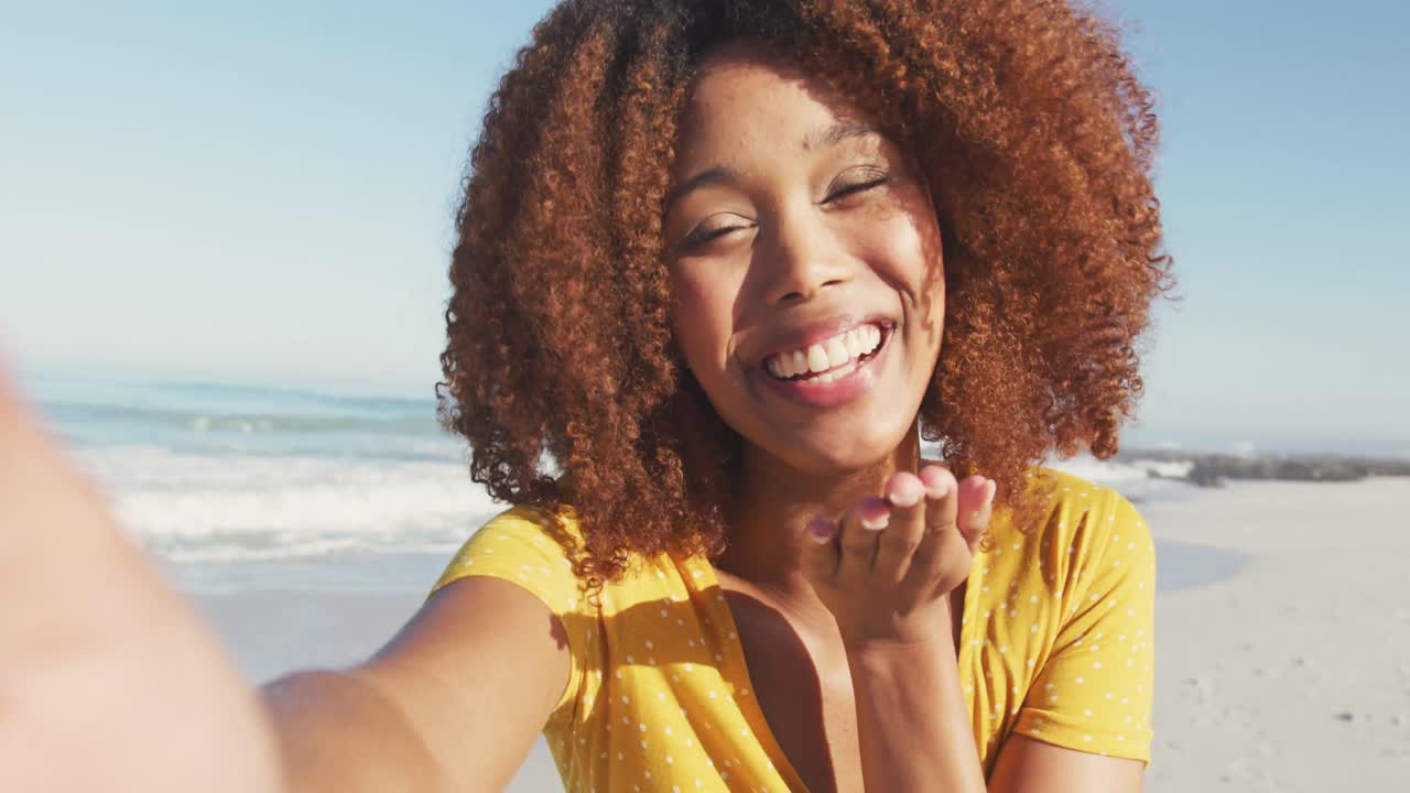 African American woman sending kisses through camera at beach