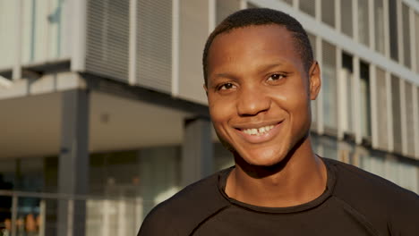 portrait of young black man smiling and looking at camera outdoors. handsome african american male athlete resting on a sunny afternoon. close-up.