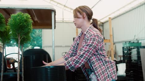 young woman working greenhouse over plant pots