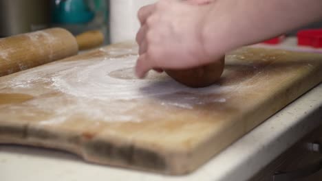 caucasian woman dusting wooden board and working on gingerbread dough with a rolling pin