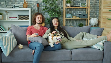 couple relaxing on sofa with dog and watching tv