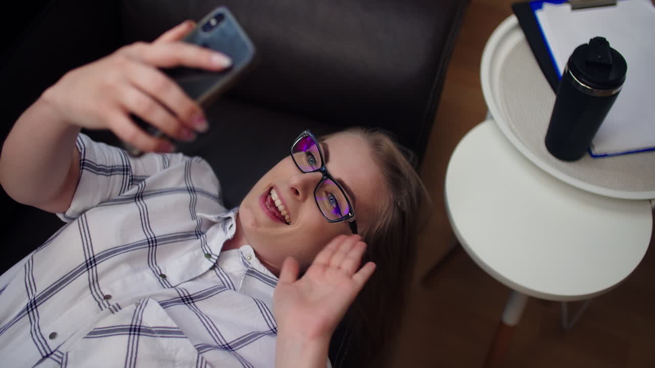 atractiva mujer de negocios que tiene una videollamada en el teléfono móvil mientras está acostada en el sofá de la oficina