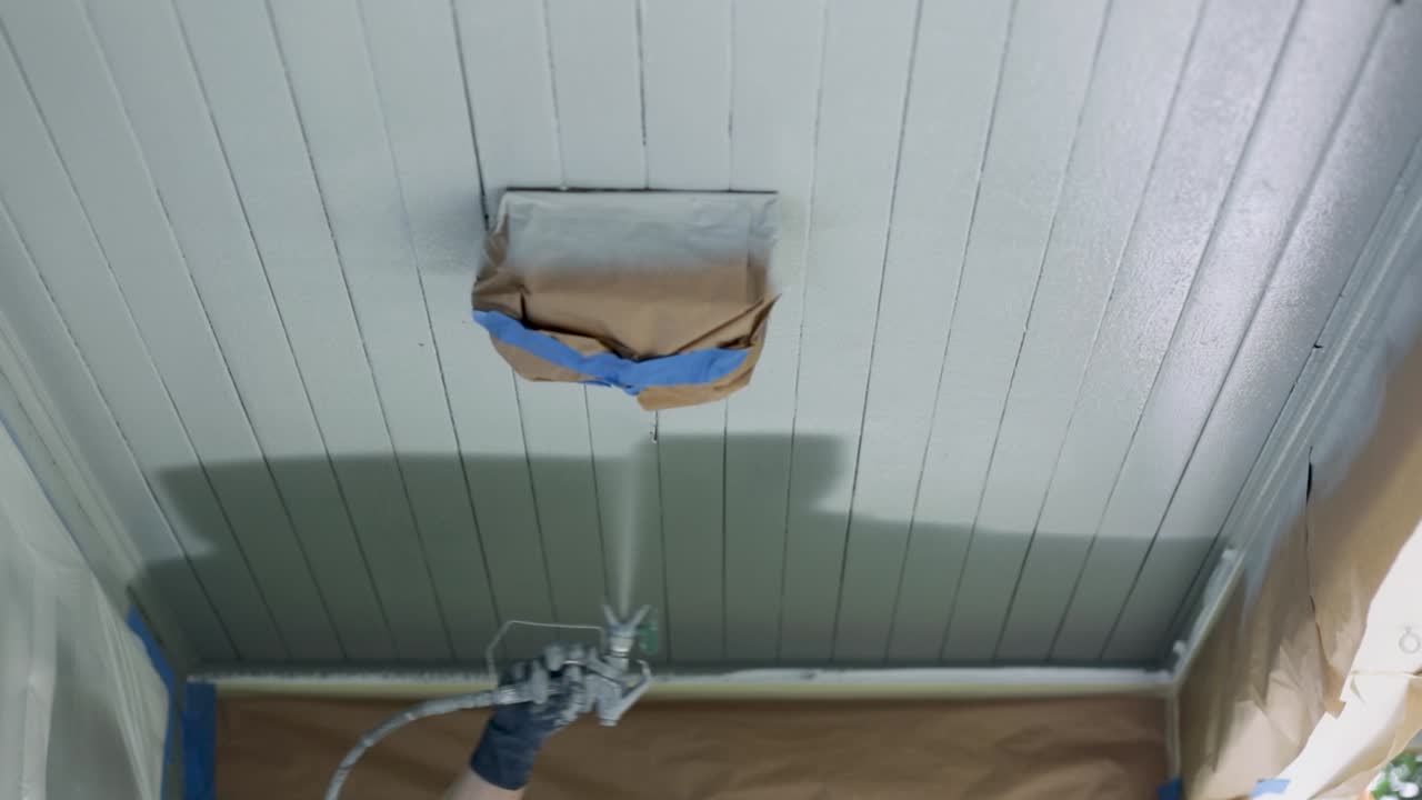 페인트 분무기를 사용하여 천장을 흰색으로 칠하는 남자