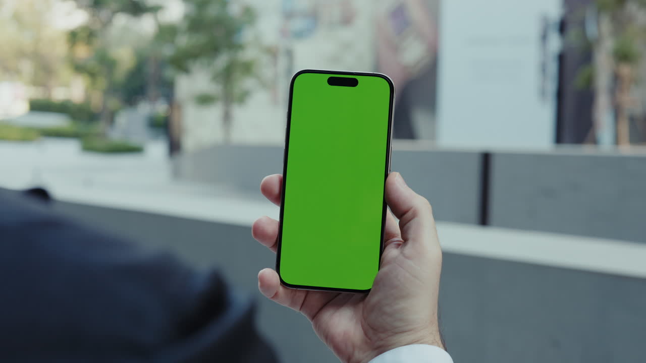 Mano che tiene uno smartphone con schermo verde in un ambiente urbano all'aperto