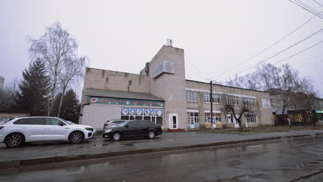 view of the street with old white-brick building and some cars parked nearby. low angle view. snow is falling on the road.