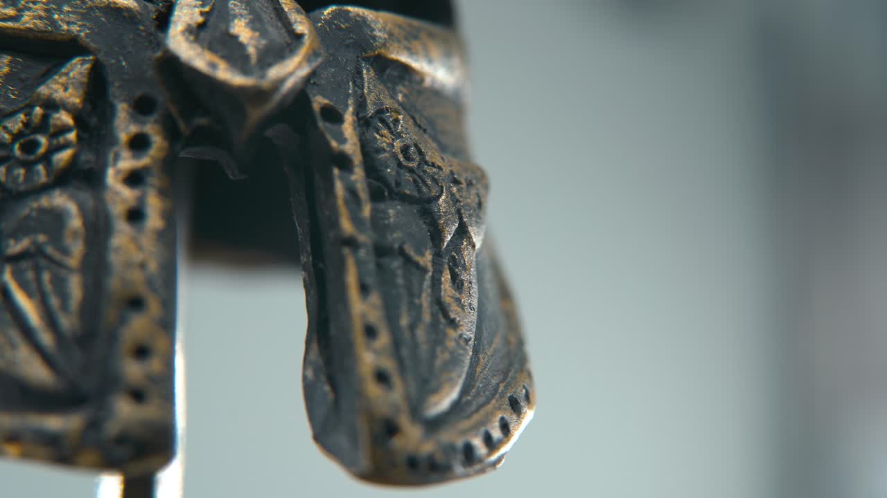 A close-up macro detailed shot of a Spartan design, two different ancient warrior metal bronze helmets, glowing textured face mask shapes, studio lighting, 4K cinematic video, Slow Motion, pan left