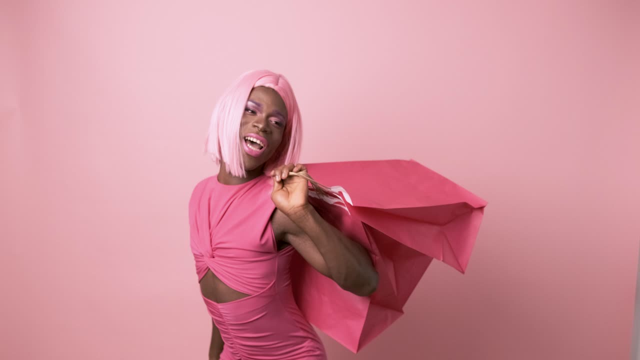 Happy transgender person with dancing holding shopping bags on pink background