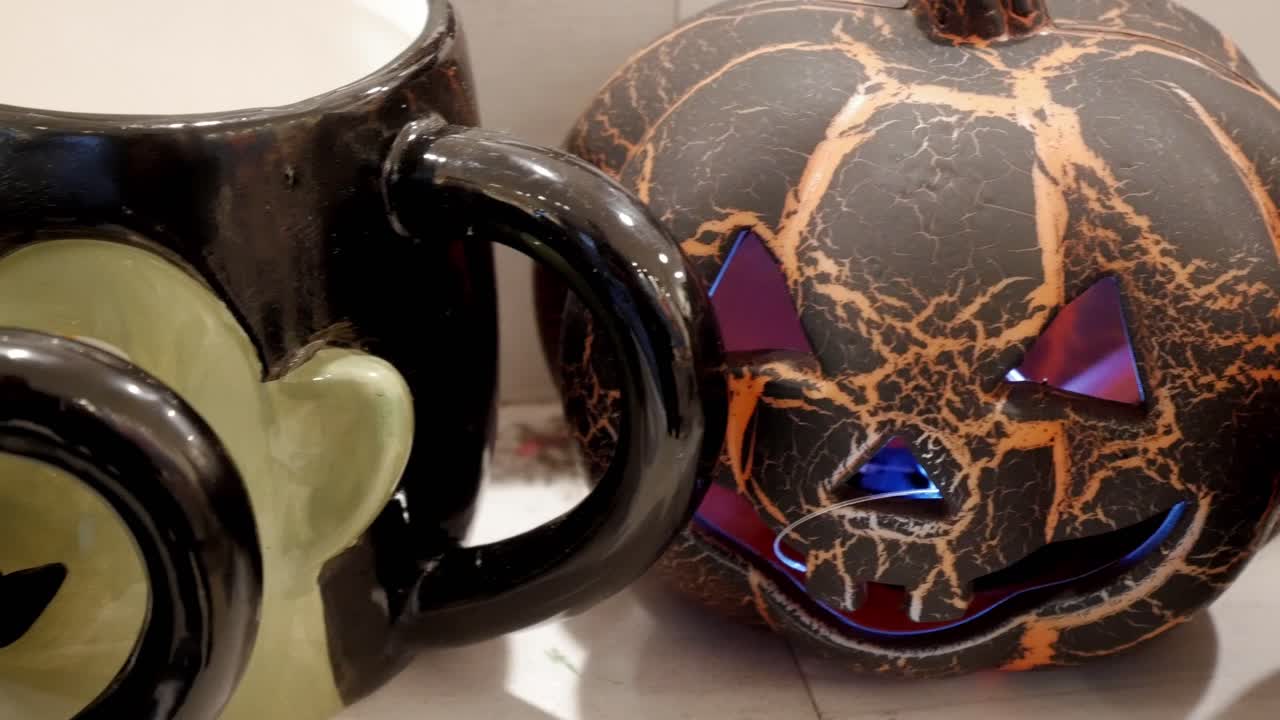 Jack'O Lantern evil looking pumkins for decoration. Black with orange stripes and blue light from inside. Frankenstein shaped mugs next to them.